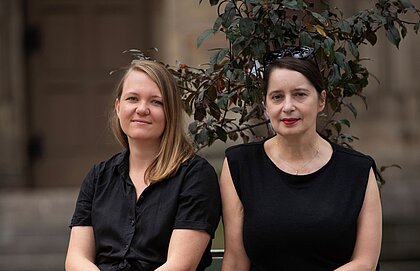 Romy Range (links) und Ania Corcilius kuratieren das Programm für "St. Maria als...". Auf dem Foto sitzen die beiden Kunstvermittlerinnen vor der katholischen Kirche St. Maria in der Tübinger Straße in Stuttgart.
