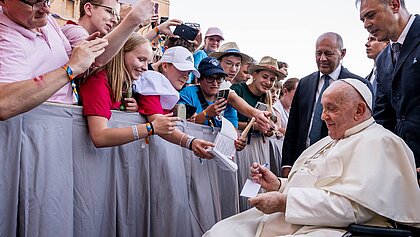 Zu sehen ist Papst Franziskus im Rollstuhl beim Weltjugendtag in Rom. Er gibt ein Autogramm. Viele der jungen Menschen machen Handybilder von dem Papst. 