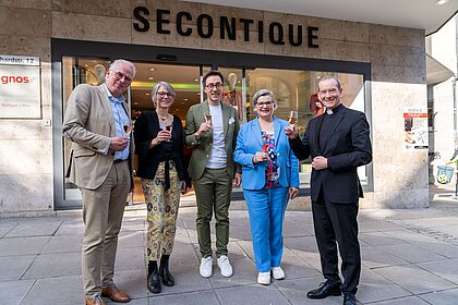 Der Vorstand des Caritasverbands für Stuttgart Raphael Graf von Deym, die Leiterin des Freiwilligenzentrums Caleidoskop Ulrike Holch, der Vorstand der Aktion Hoffnung Anton Vaas, die Bereichsleiterin Second Hand Shops der Aktion Hoffnung Regina Hagmann-Kuttruf und Christian Hermes stoßen vor der Secontique in der Eberhardstraße auf die Neueröffnung der nachhaltigen Boutique an. 