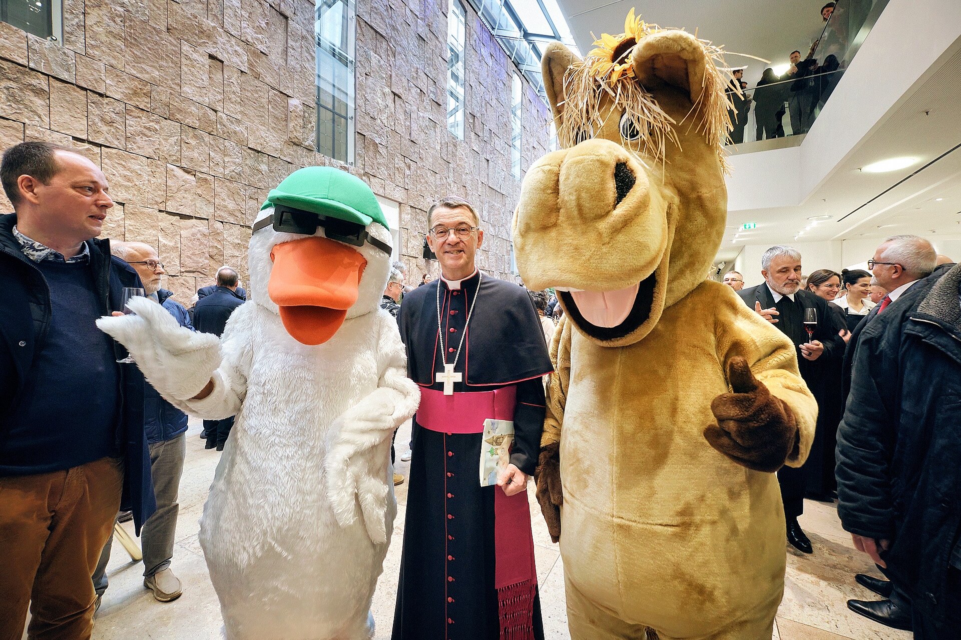 Beim Stehempfang für den neuen Bischof im Haus der Katholischen Kirche waren auch die beiden diözesanen Maskottchen Roxy Ross und Gani Gans dabei, die den Bischof in ihre Mitte genommen haben. 