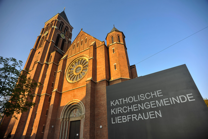 Zu sehen ist die katholischen Liebfrauenkirche in Bad Cannstatt im Sonnenlicht. Auf dem Schild davor ist zu lesen: Katholische Kirchengemeinde Liebfrauen. 