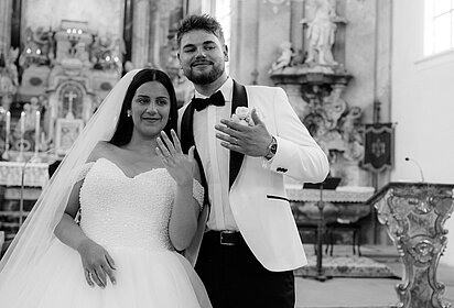 Marie und Bennet Schramm bei ihrer Hochzeit in der Kirche; beide halten ihre Hand mit dem Ehering hoch