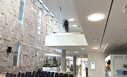 Ein Blick in das lichtdurchflutete Haus der Katholischen Kirche mit Sandsteinwand, Stühlen und der Infotheke 